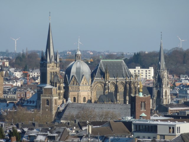 Symbolbild Aachen: In der Ferne ist der imposante Aachener Dom zu sehen, ein herausragendes Beispiel mittelalterlicher Architektur. Neben ihm erhebt sich der Turm der Pfarrkirche St. Foillan, ein weiteres charakteristisches Wahrzeichen der Stadt. Diese Darstellung vermittelt die historische und kulturelle Bedeutung von Aachen durch die beeindruckende Silhouette seiner sakralen Bauwerke.