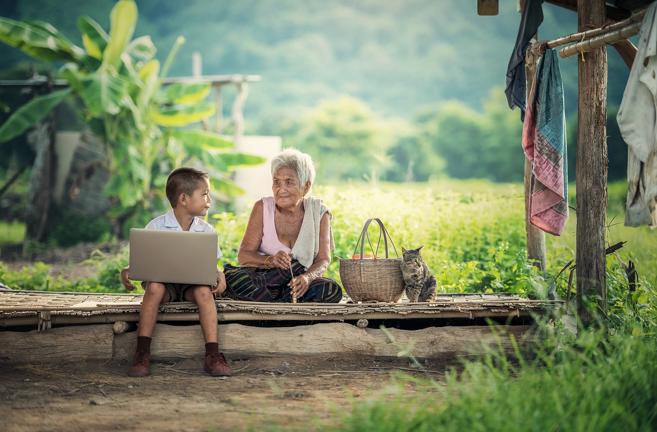 Hintergrundbild zum Thema lebenslanges Lernen: Ein Kind und eine Greisin sitzen nebeneinander, das Kind hält einen Laptop auf dem Schoß. Der Blickkontakt zwischen den beiden deutet auf eine gemeinsame Auseinandersetzung oder das Erklären von Wissen hin, was die kontinuierliche Bedeutung des Lernens über alle Lebensphasen verdeutlicht.